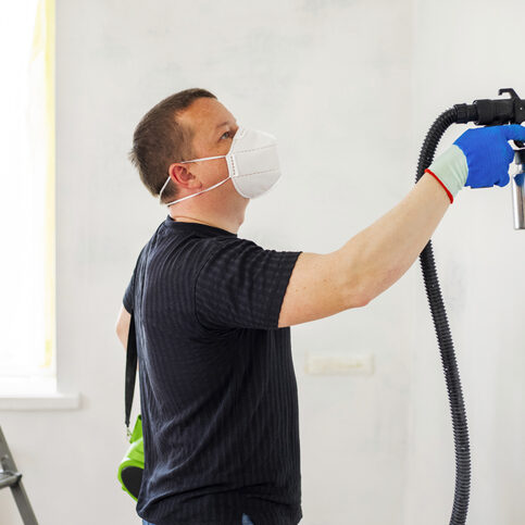 Man in protective mask paint a wall with an electric spray gun Man in protective mask paint a wall with an electric spray gun. Electric spray painting. Repair of the apartment